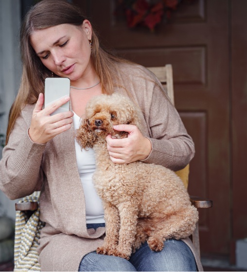 Pet owner using smartphone for telehealth vet consultation while holding dog at home Plainsboro, NJ